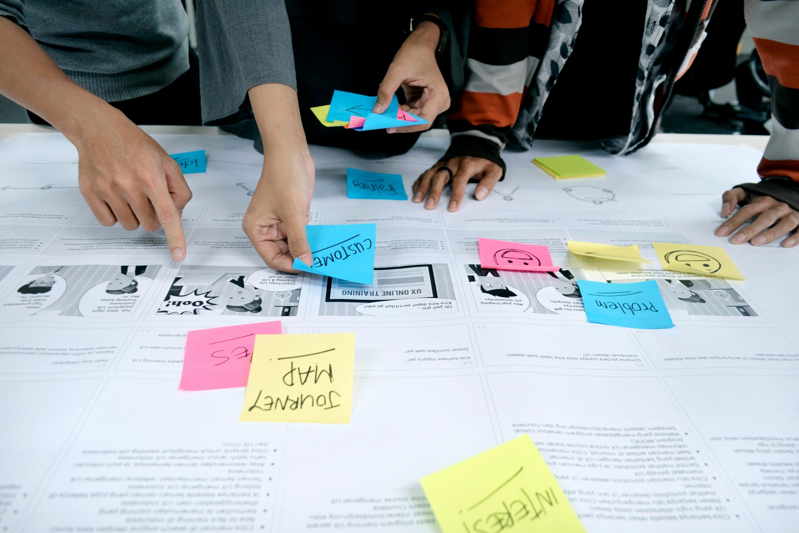 Mãos de uma equipe diversa colaborando em brainstorming, organizando post-its coloridos com ideias em uma mesa de trabalho.