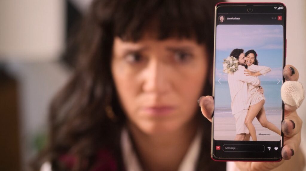 Vicky, personagem da série Invejosa da Netflix, mostra o celular com expressão de decepção ao ver o ex com a nova namorada