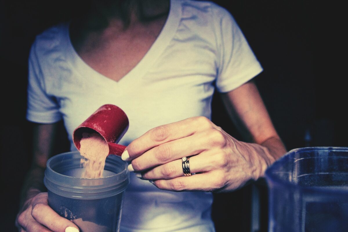 Mulher preparando shake de whey protein na cozinha, representando o modismo da proteína e dietas da moda.
