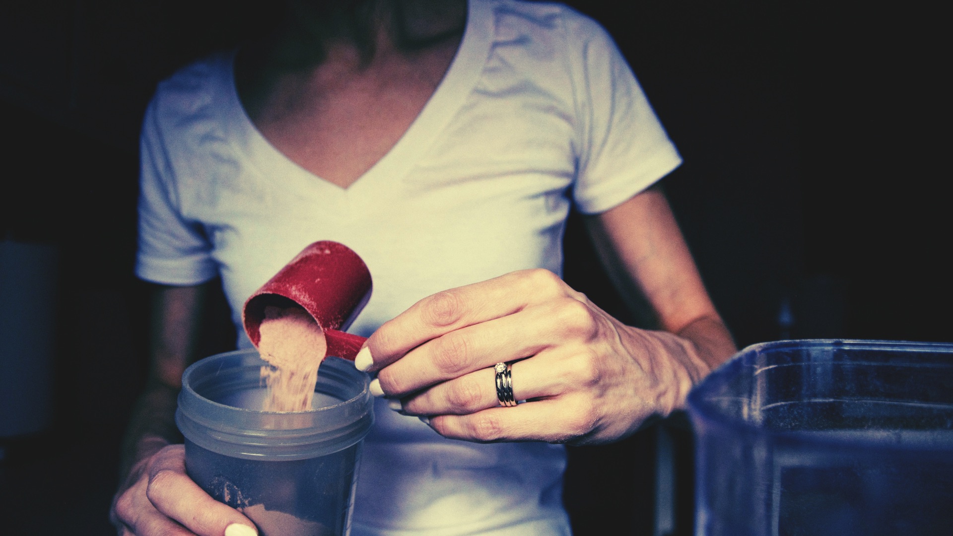 Mulher preparando shake de whey protein na cozinha, representando o modismo da proteína e dietas da moda.